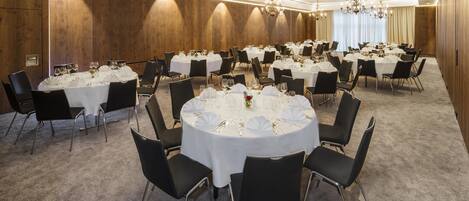 A conference room with round tables, black chairs, and chandeliers.