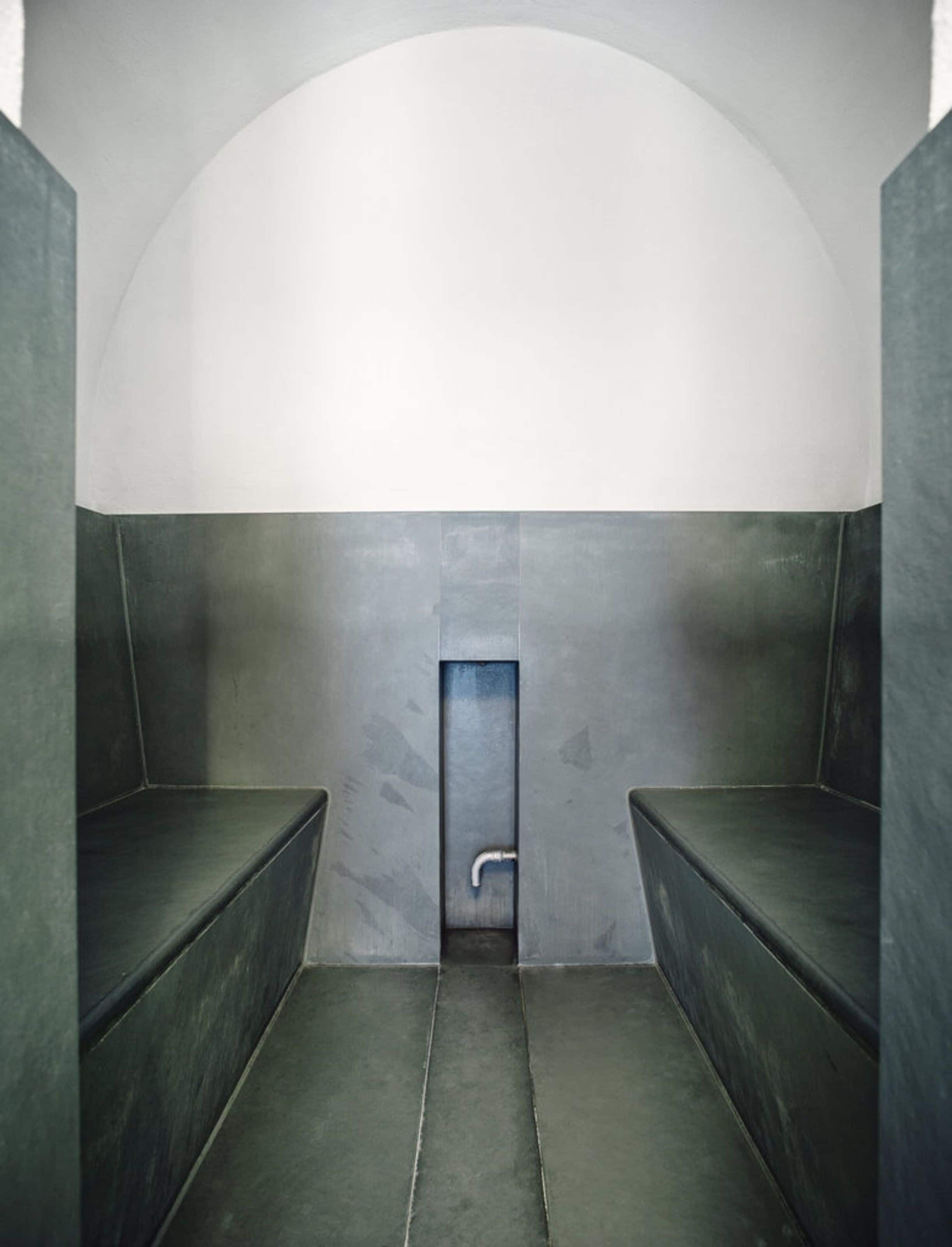 A modern, minimalist bathroom with a curved ceiling, dark walls, and a central door.