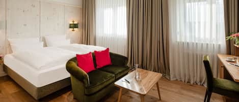 Una habitación de hotel con una cama, un sofá verde con cojines rojos, una mesa de madera y una silla.