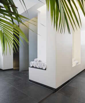 Een moderne lobby met een receptiebalie, een zithoek met handdoeken en een grote potplant.