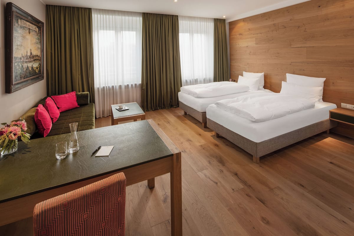 Een hotelkamer met twee bedden, een eettafel, een stoel en een schilderij aan de muur.