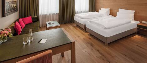 A hotel room with two beds, a dining table, a chair, and a painting on the wall.