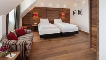 Un dormitorio moderno con techo estilo loft, dos camas individuales, un sofá a rayas con cojines rojos, piso de madera y una pequeña mesa con un jarrón de flores.