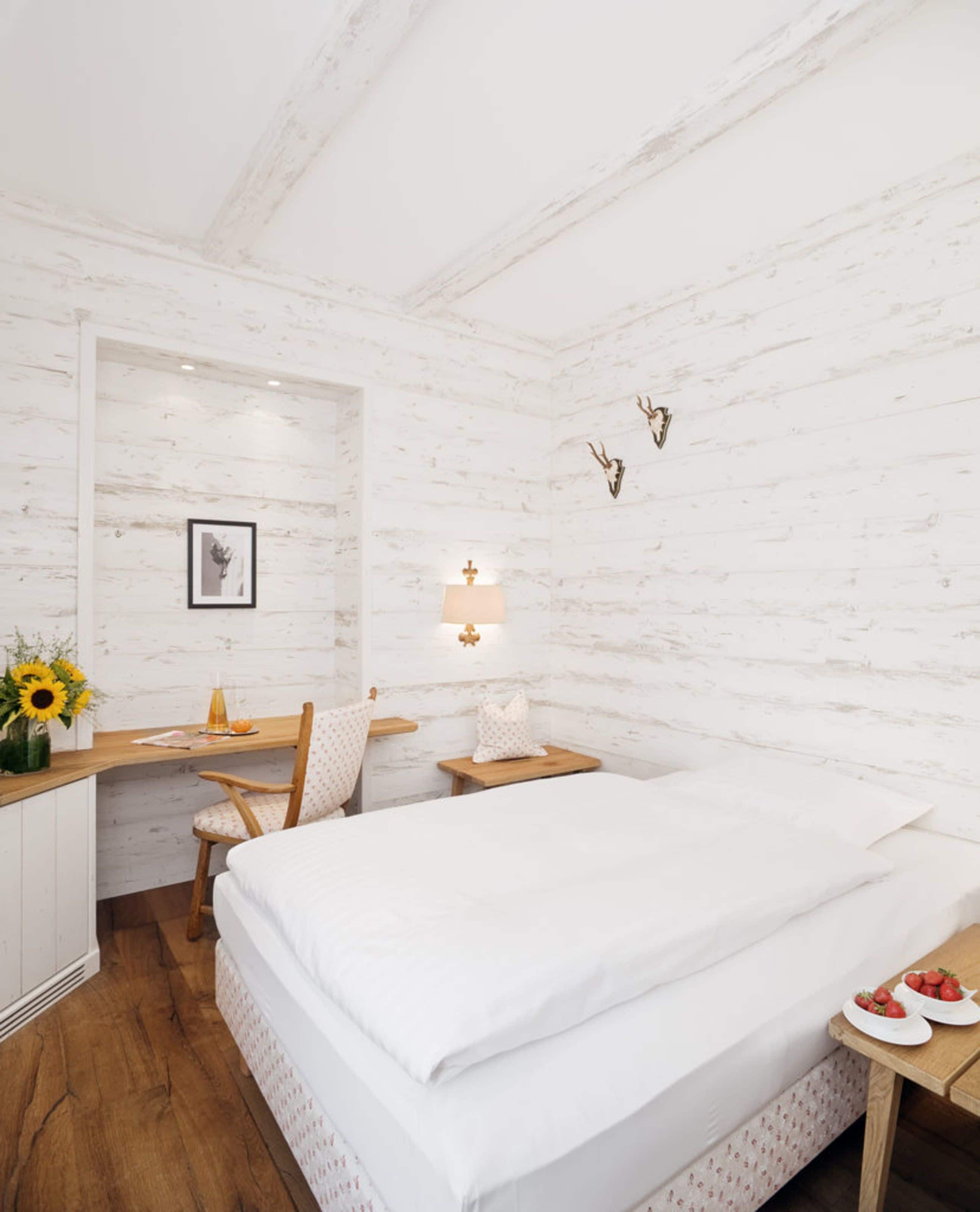 Une chambre à coucher comprenant un lit, un bureau, une chaise, une table de chevet, une lampe, un tableau accroché au mur et une décoration murale représentant une tête de cerf.
