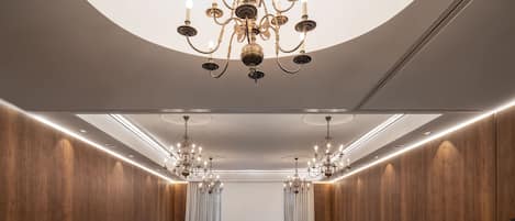 A conference room with a large chandelier, wooden panel walls, and rows of black chairs.