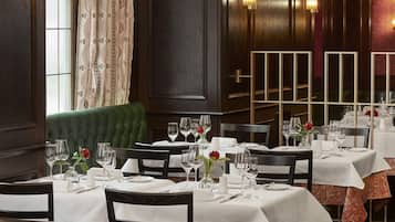 A restaurant with multiple tables set for dining, featuring white tablecloths and red roses as centerpieces.