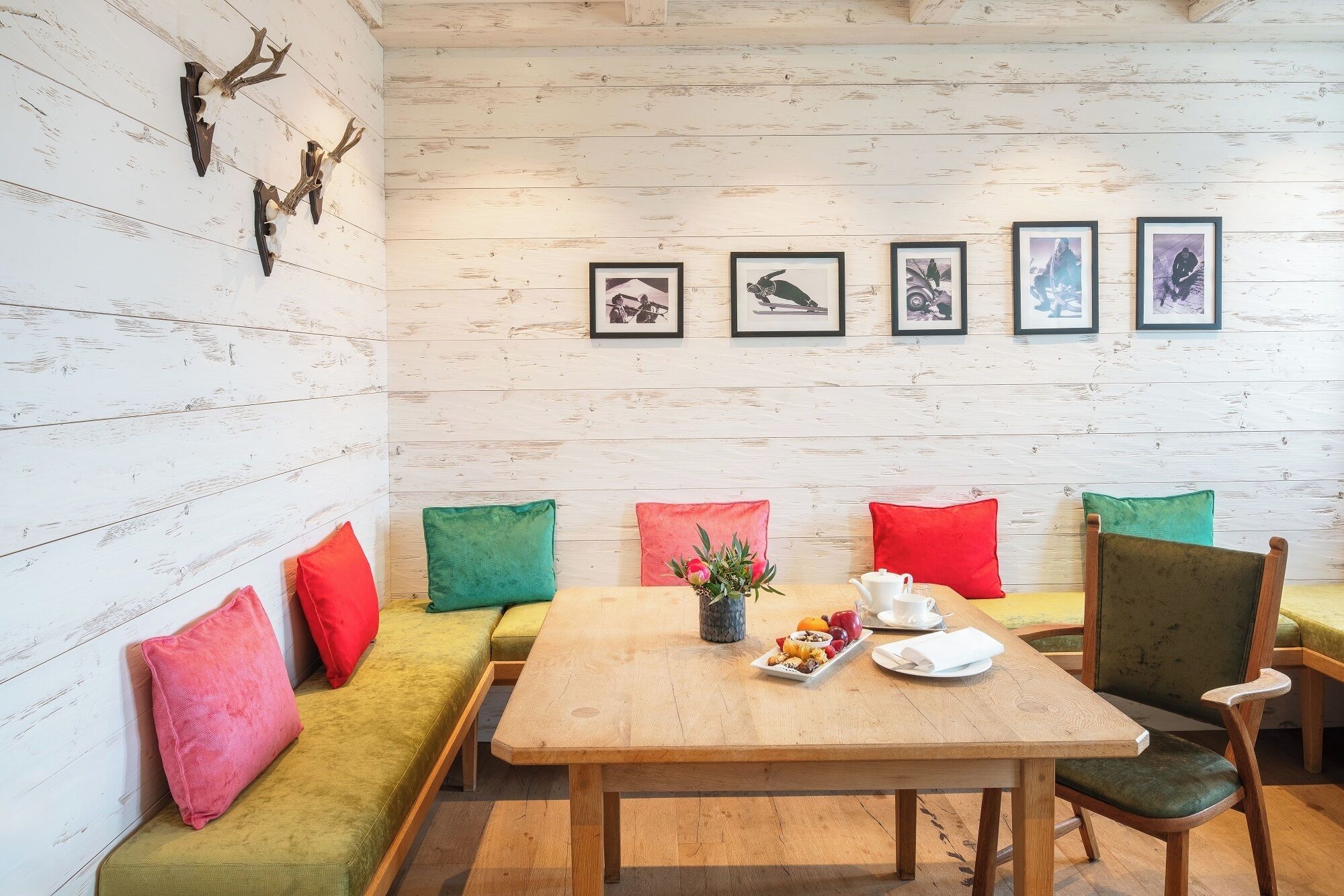 A room with a wooden wall, a sofa, a dining table with a fruit platter, and framed pictures on the wall.