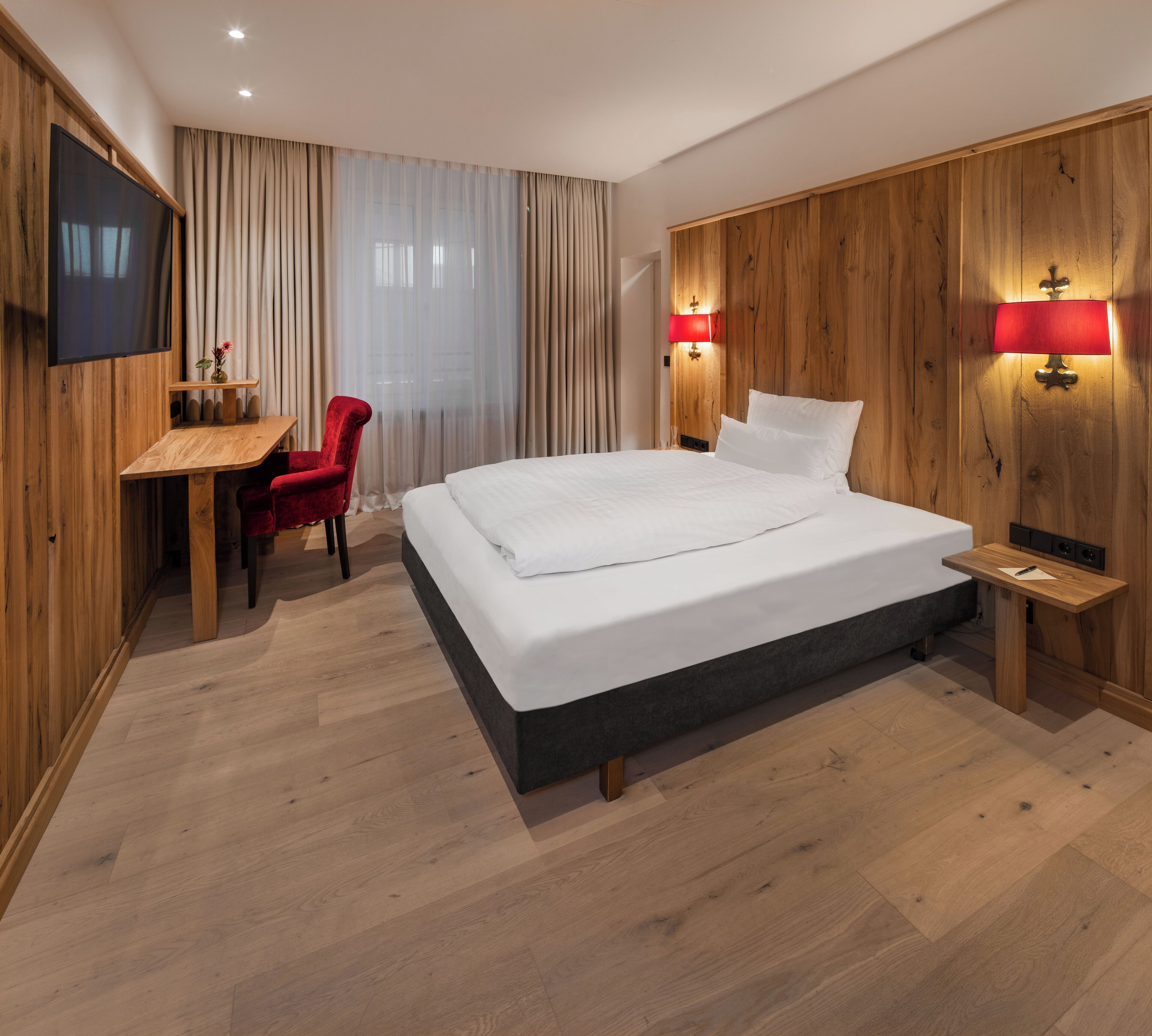 Una habitación de hotel moderna con una cama grande, paneles de madera, un escritorio con una silla y dos lámparas de noche.
