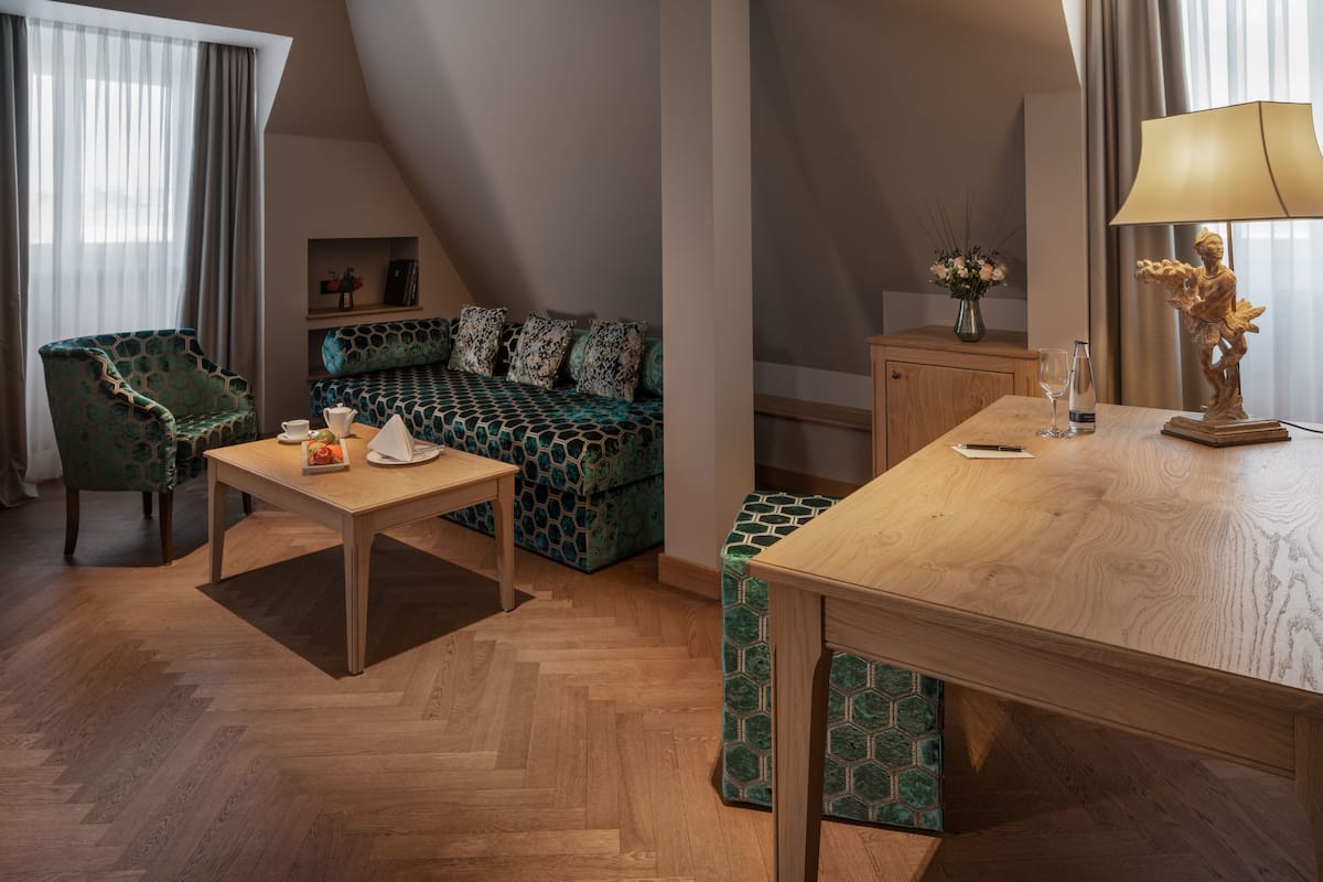 Een gezellige kamer met een houten eettafel, een groene bank met patroon, een groene fauteuil en een klein kastje met een bloevas.