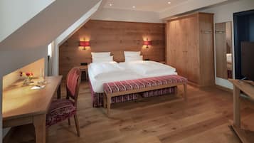 A bedroom with a wooden headboard, a bed with white bedding, a wooden desk with a chair, and a television on a stand.