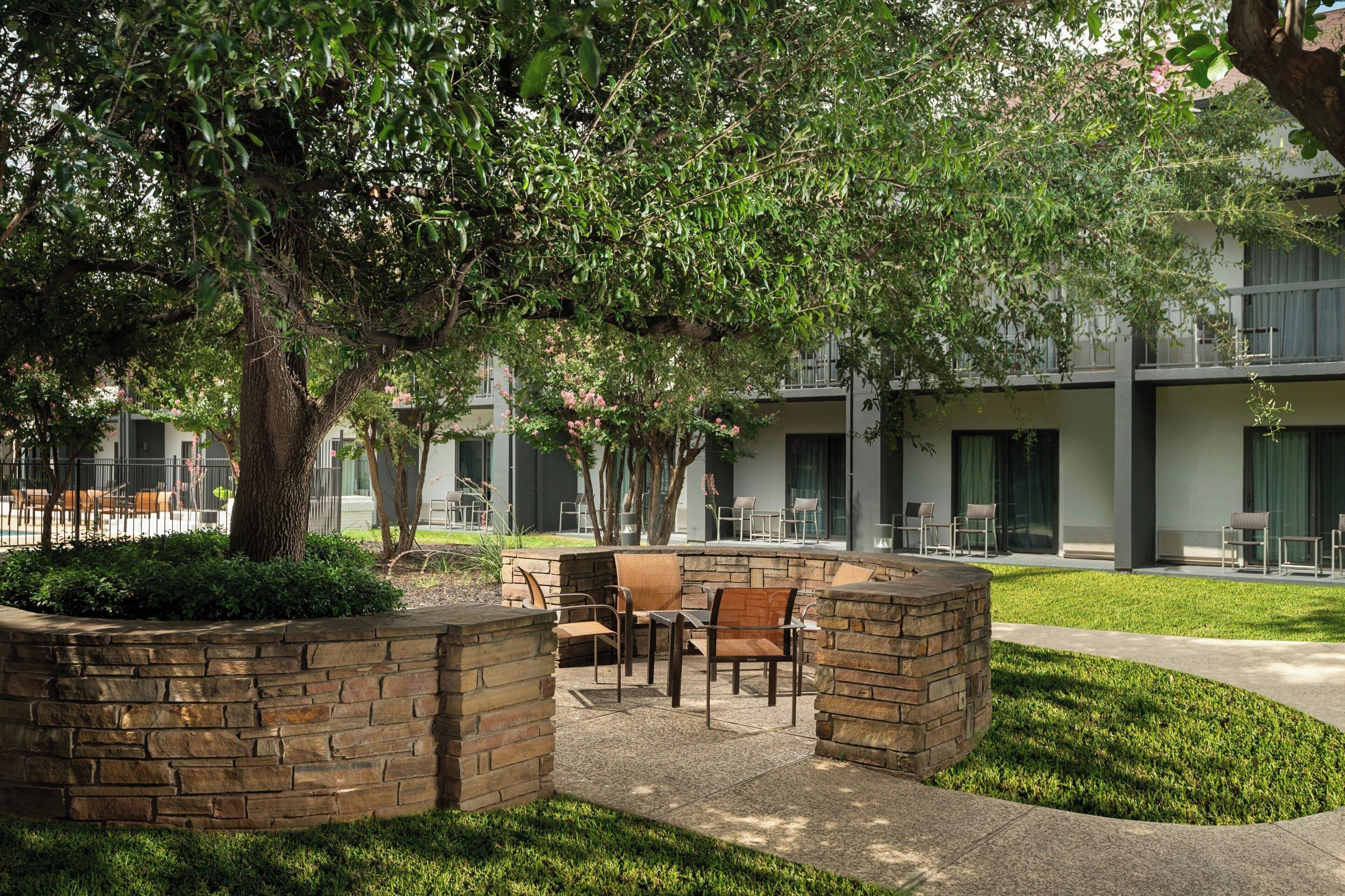An outdoor seating area with stone planters, a large tree, and a building in the background.