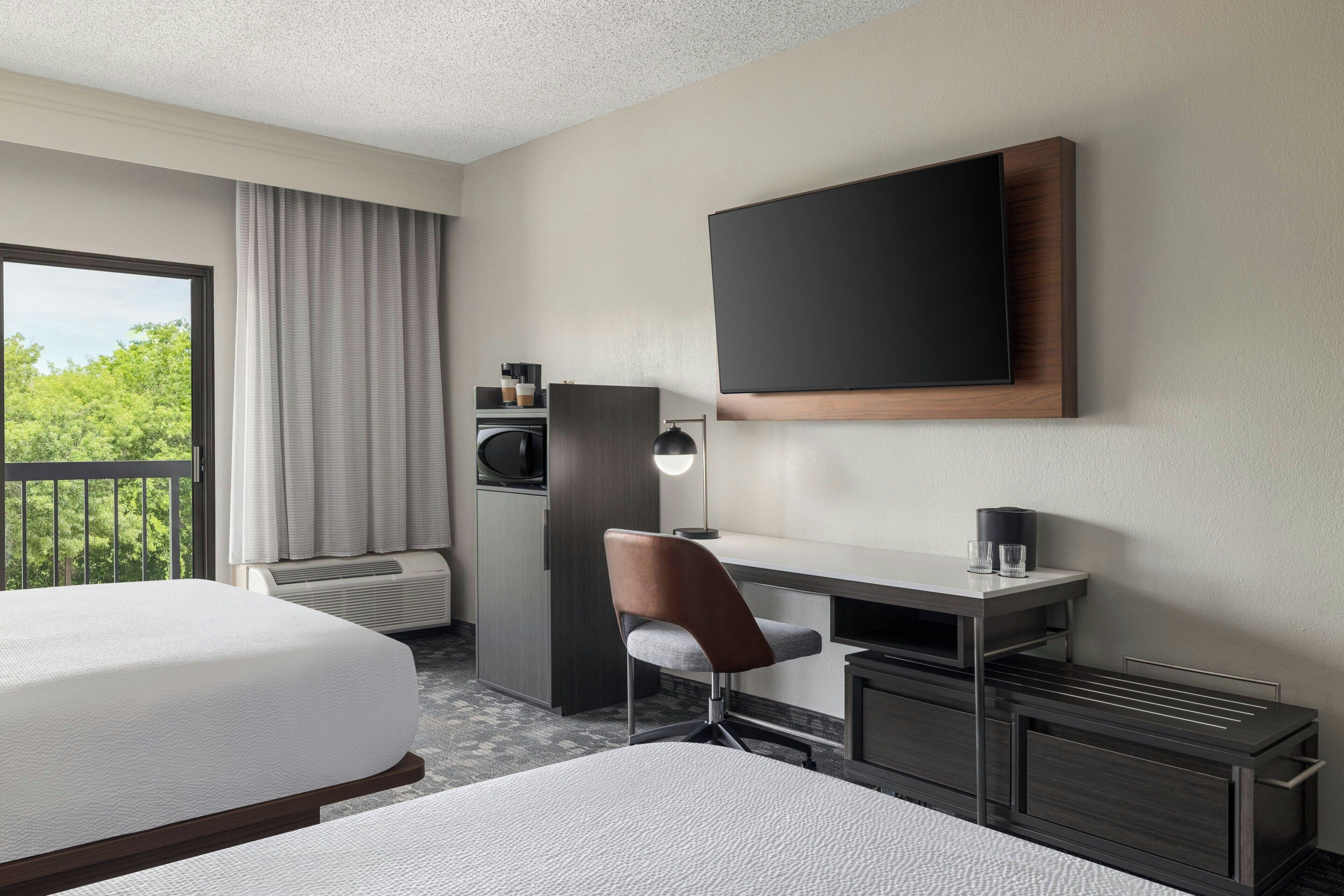 Habitación de hotel con cama, escritorio, silla, televisión y vistas a zonas verdes.