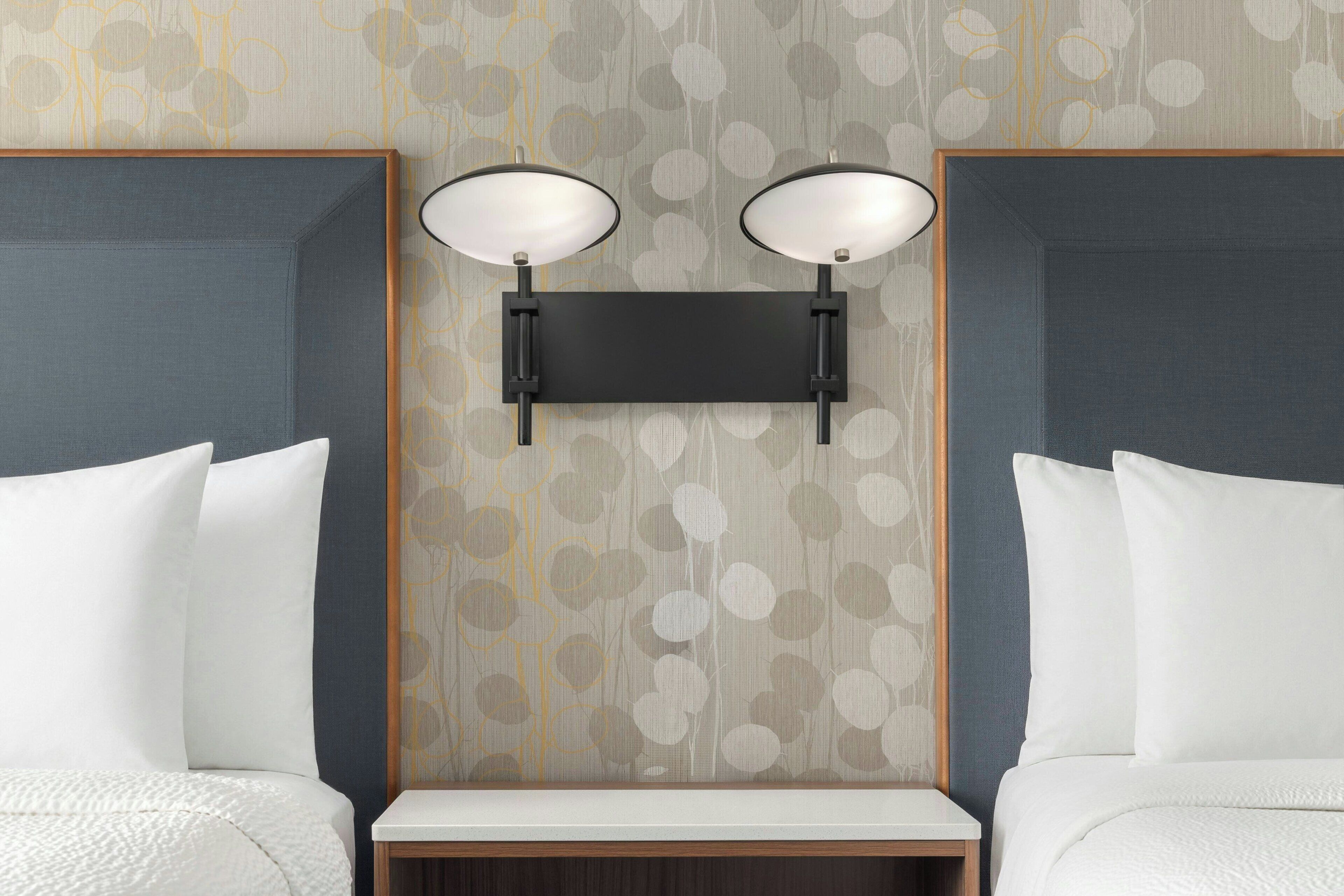 Une chambre d’hôtel avec deux lits, une table de chevet et un luminaire fixé au mur.