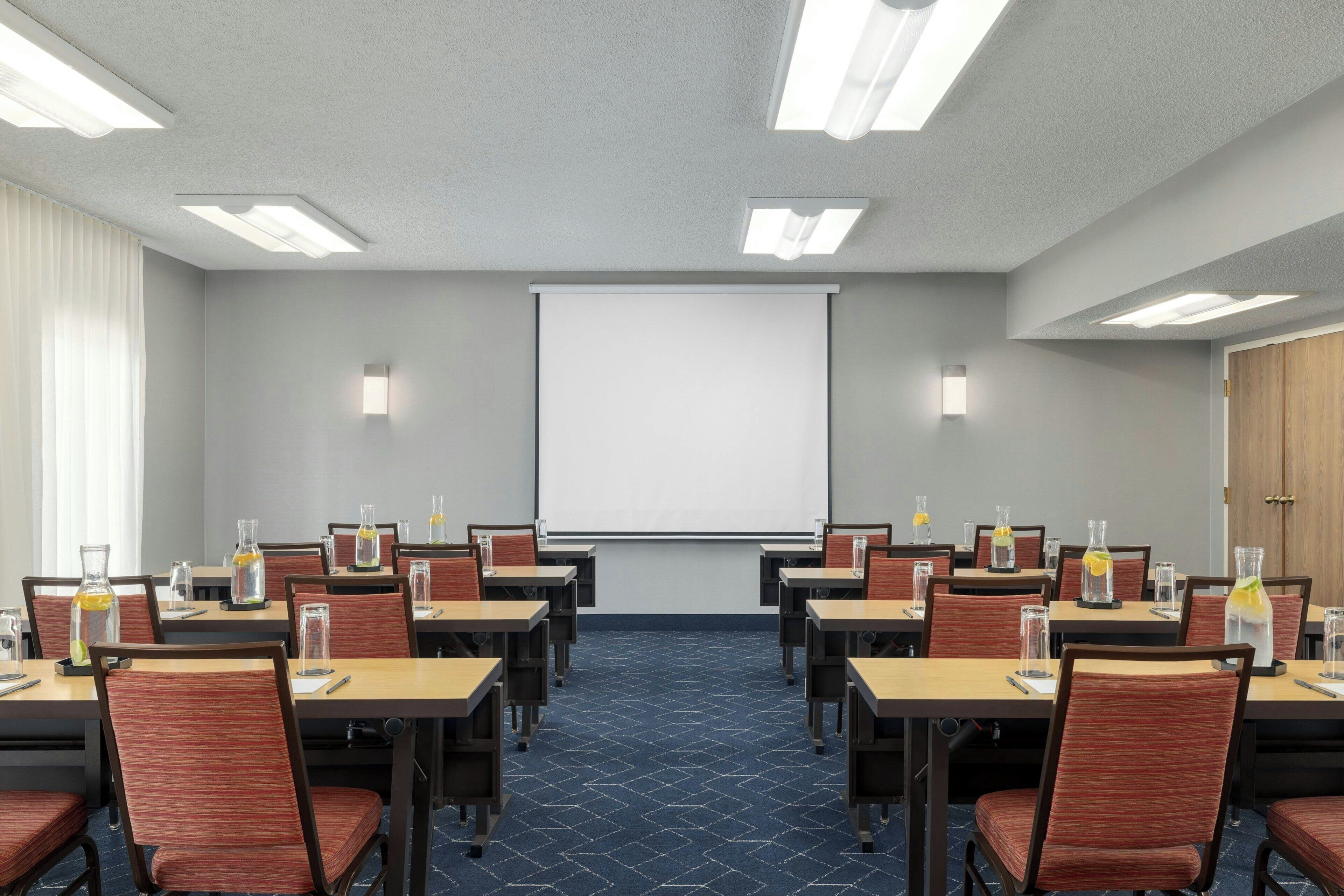 A conference room with tables, chairs, a projector screen, and a carpeted floor.