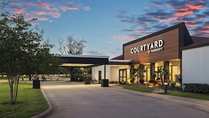 Un hôtel Courtyard by Marriott au design moderne, doté d’un espace extérieur couvert et d’un aménagement paysager bien entretenu.