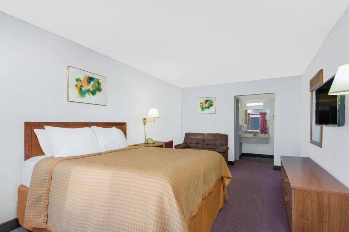 A hotel room with a bed, a desk, a chair, a TV, and artwork on the walls.