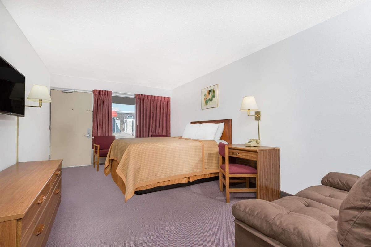 Ein Hotelzimmer mit Bett, Schreibtisch, Stuhl, Sofa, Fernseher und einem fensterbepflanzten Fenster.