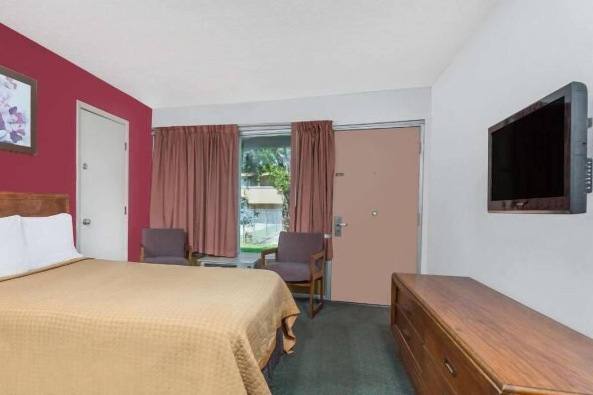 A hotel room with a bed, a desk, two chairs, a television, and a door.