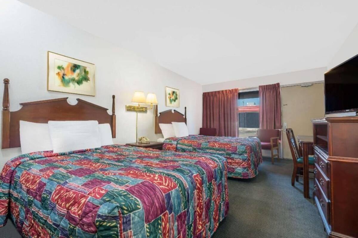 A hotel room with two beds, a desk, a chair, a dresser, and a television.