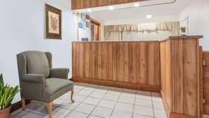 Una zona de recepción con un mostrador de madera, un sillón verde e impresión botánica enmarcada en la pared.