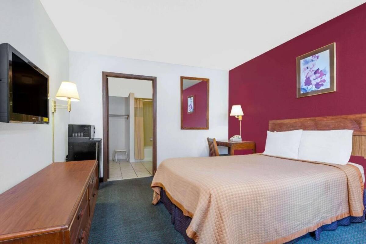 A hotel room with a bed, a desk, a TV, and a door leading to a bathroom.