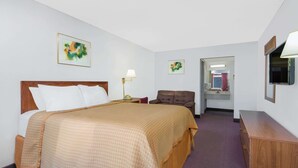Habitación de hotel con cama, escritorio, silla, espejo y televisor.