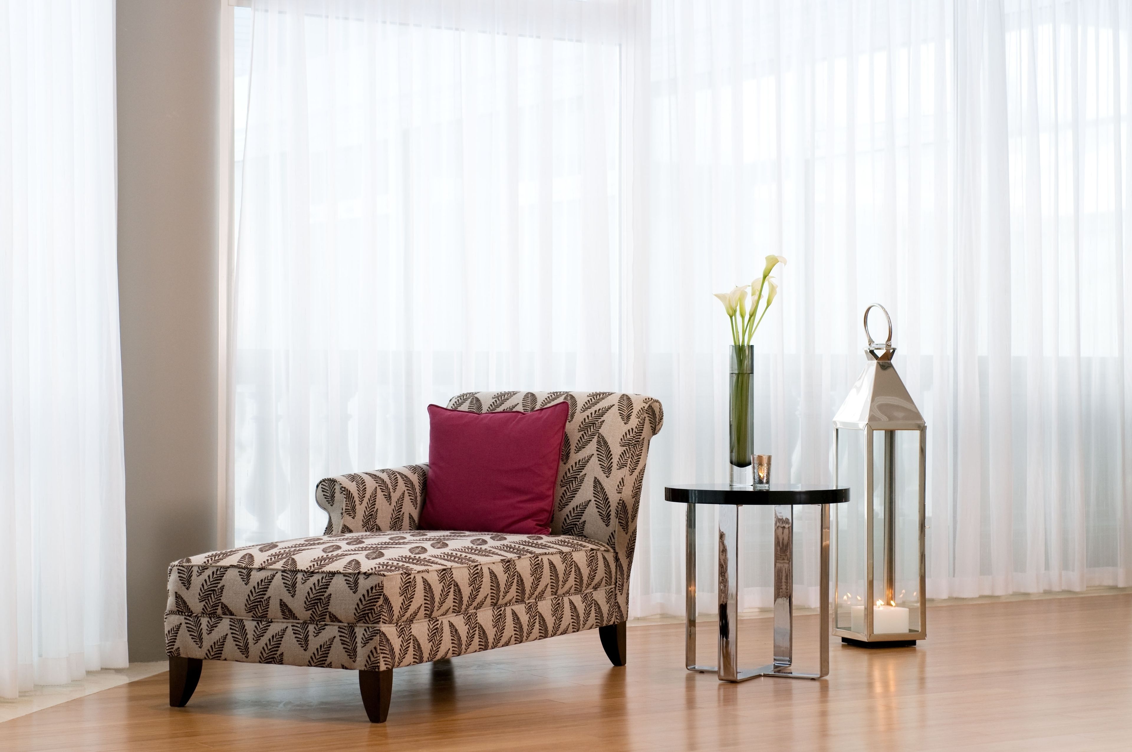 Una habitación con un sillón estampado, una mesita con una vela y un farol.