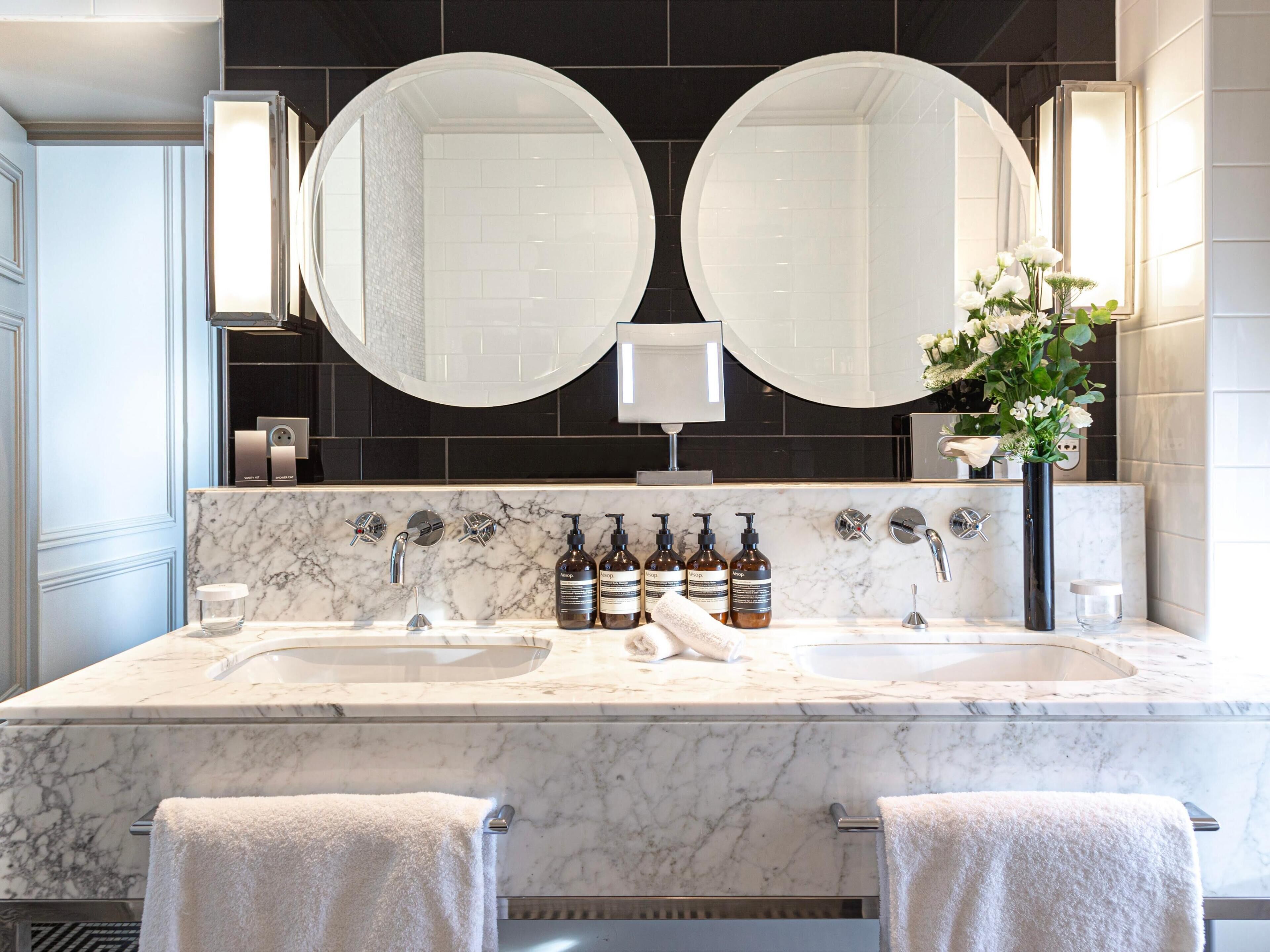 A bathroom with two sinks, a large mirror, and a vase with flowers.