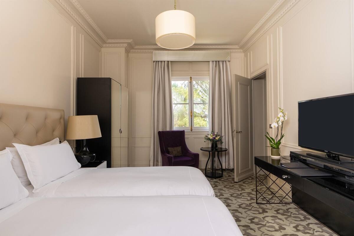 Une chambre d’hôtel avec un grand lit, une télévision, un bureau avec un ordinateur, une chaise et une fenêtre avec des rideaux.