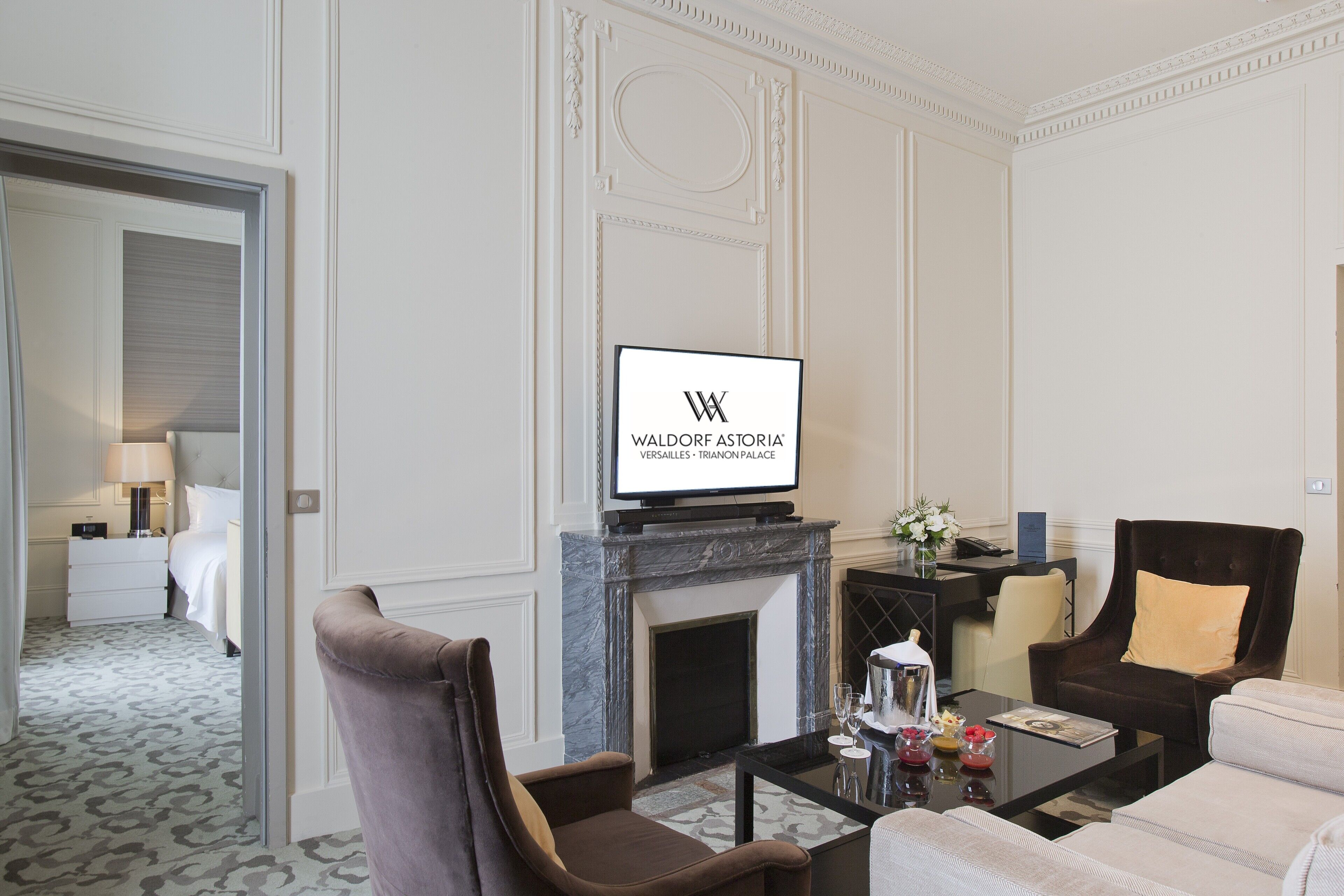 A hotel room with a fireplace, a television mounted above it, a sofa, a coffee table, and a chair.