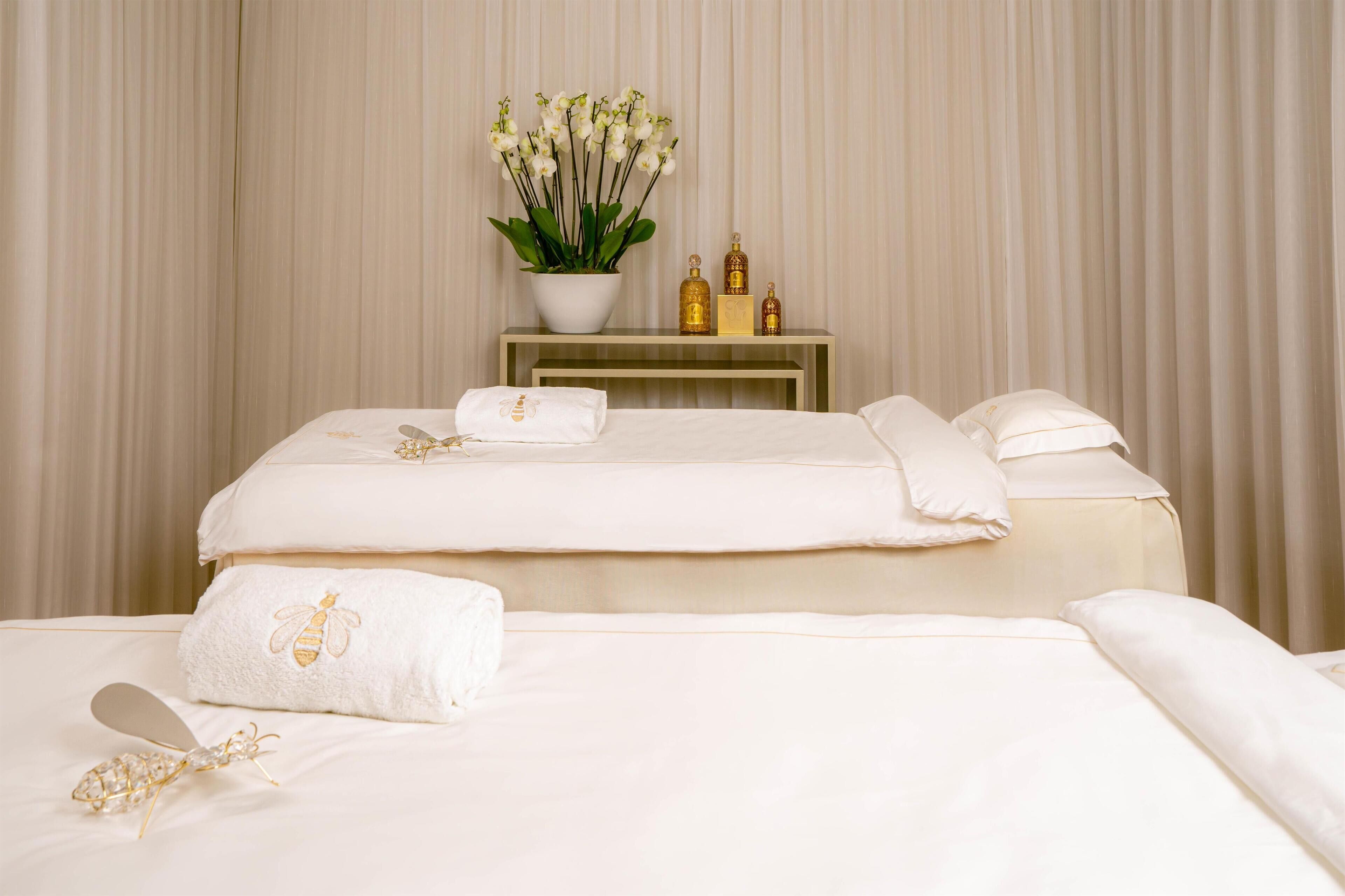 A hotel room with a bed, a bedside table with a vase of flowers, and a nightstand with toiletries.