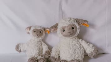 Two plush sheep toys on a white bed with a tufted headboard.