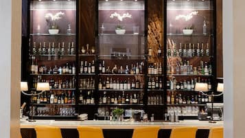 Un espace bar avec un mur en marbre, des étagères remplies de bouteilles d’alcool et des chaises jaunes.