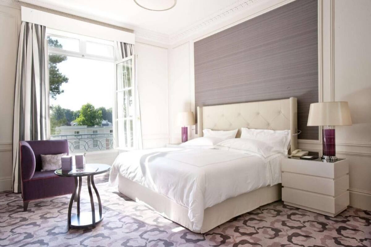Une chambre d’hôtel avec un lit, une chaise, une table de chevet et une fenêtre avec des rideaux.