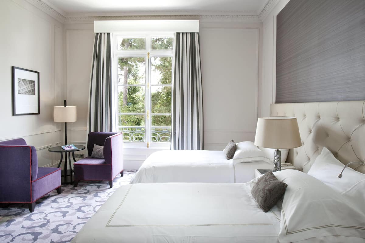 Une chambre d’hôtel avec deux lits, une chaise, une petite table et une lampe.