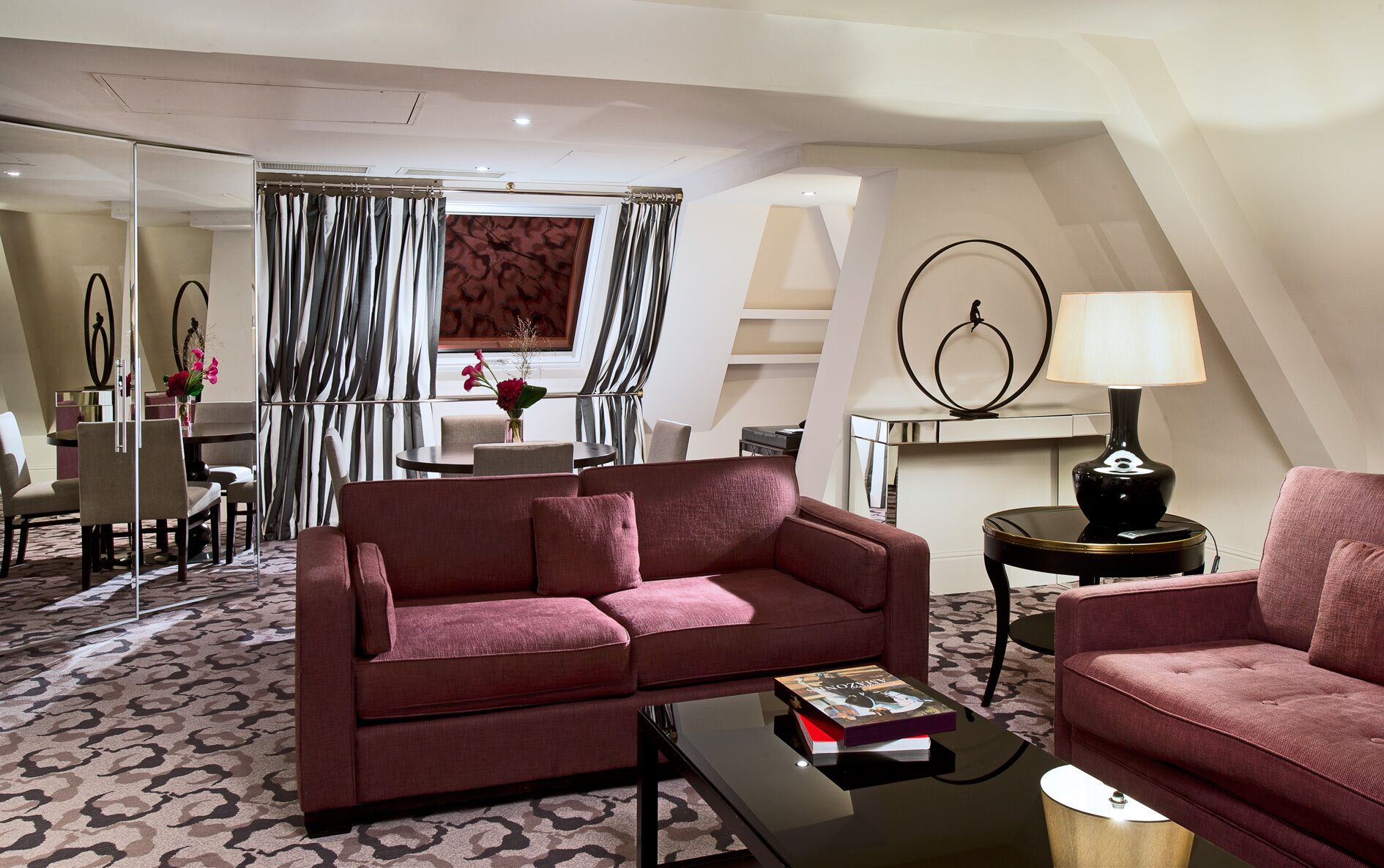 A modern living room with a red sofa, a coffee table, and a lamp. There is a dining area with a table and chairs in the background.