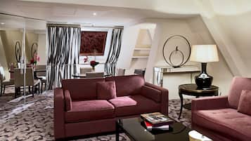 A modern living room with a red sofa, a coffee table, and a lamp. There is a dining area with a table and chairs in the background.