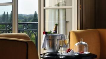 Une table à manger avec une bouteille de champagne, des verres et un plat couvert, le tout placé devant une fenêtre donnant sur un paysage verdoyant.