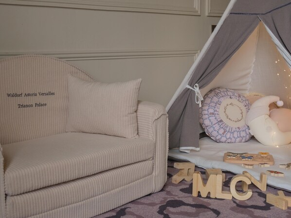 Ein gemütliches Zimmer mit einem beigefarbenen Sofa, einem bettähnlichen Sitzplatz mit Kissen und Holzbuchstaben auf dem Boden.