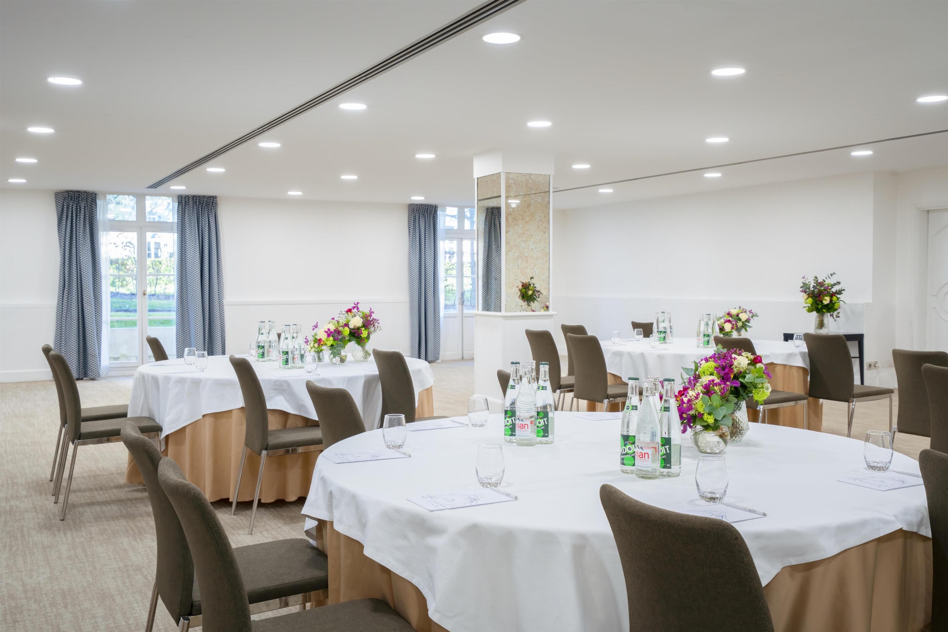 Une salle de conférence équipée de tables rondes, de chaises et agrémentée de compositions florales.