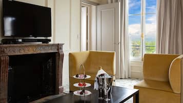 Una habitación con televisión de pantalla plana, chimenea, un sillón amarillo, una mesita con una botella de champán y copas, y vistas al balcón.