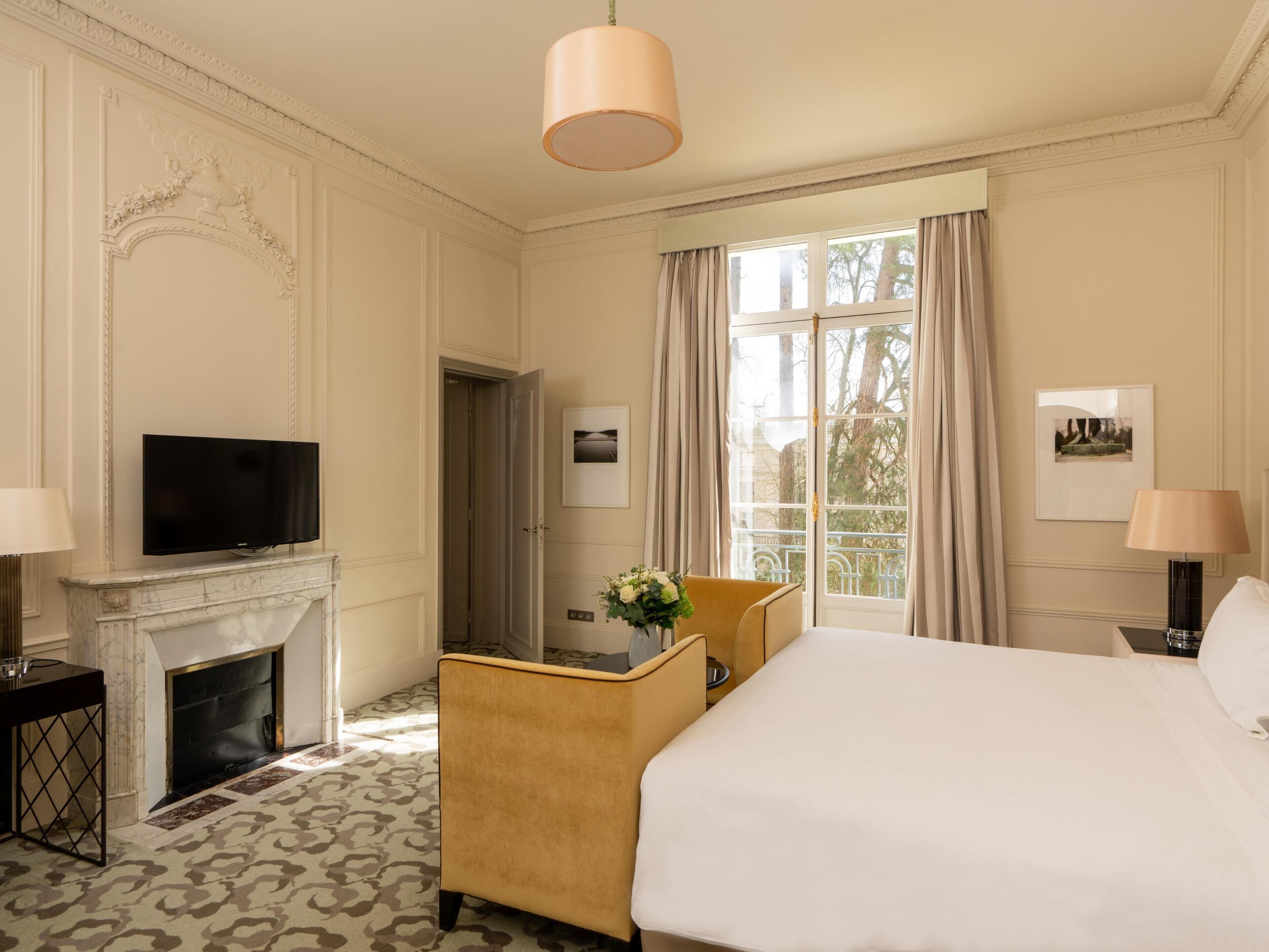 A hotel room with a bed, a television, a fireplace, a desk, and a window with curtains.