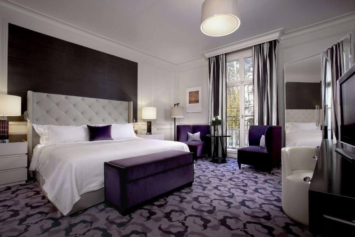 Une chambre d’hôtel avec un grand lit, un coin salon, une télévision et une fenêtre avec des rideaux.