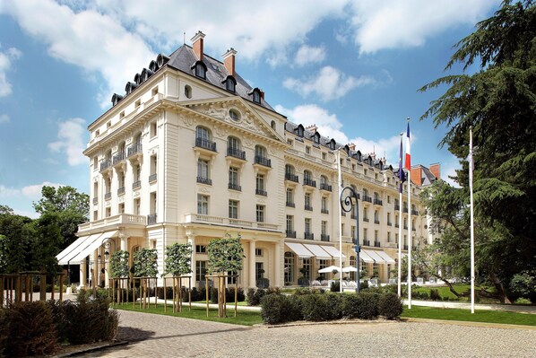 A large, historic building with multiple balconies, a flagpole with flags, and a well-maintained garden area.