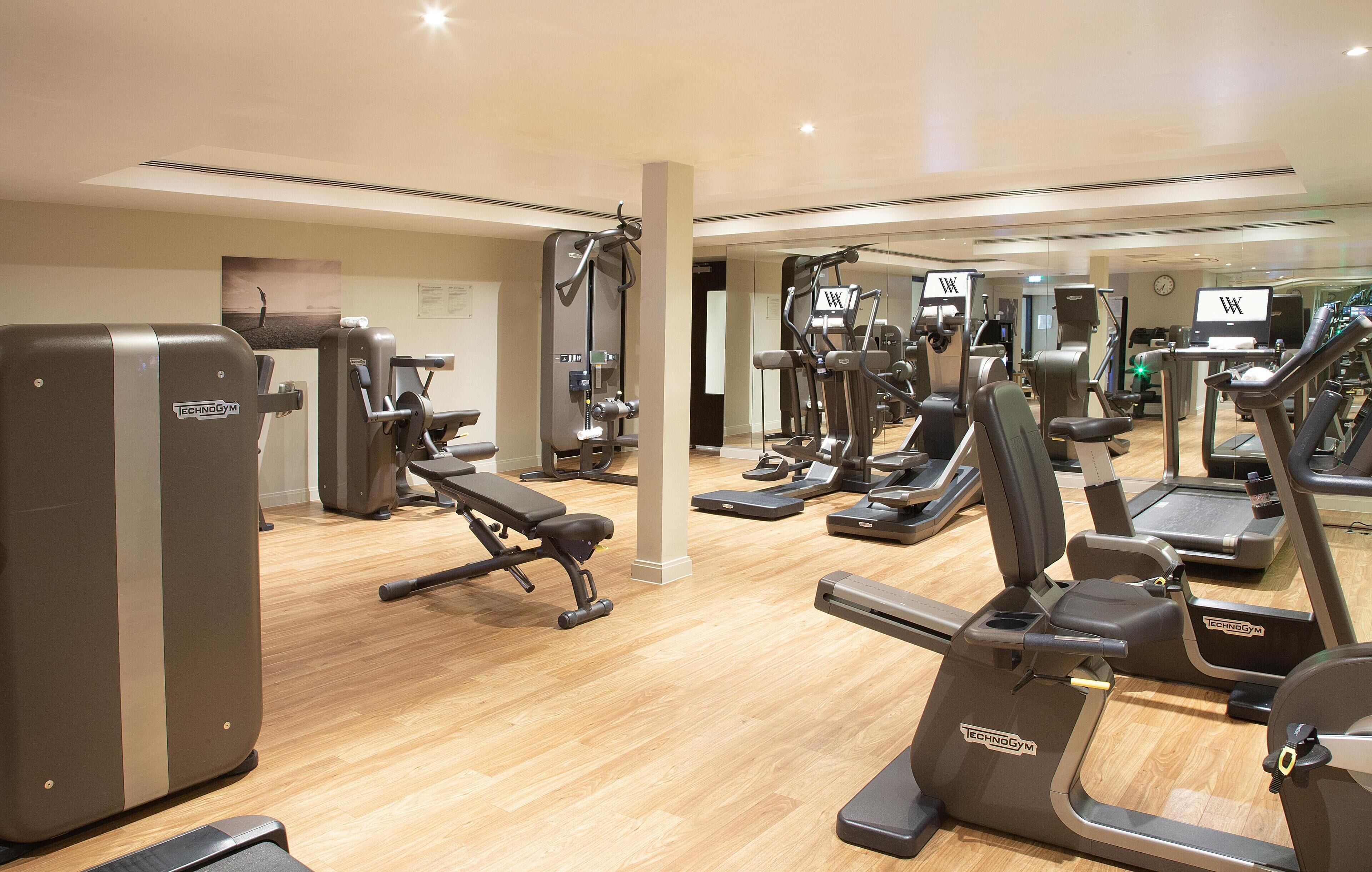 A gym with various exercise machines, including treadmills and weight machines, arranged in a spacious layout.