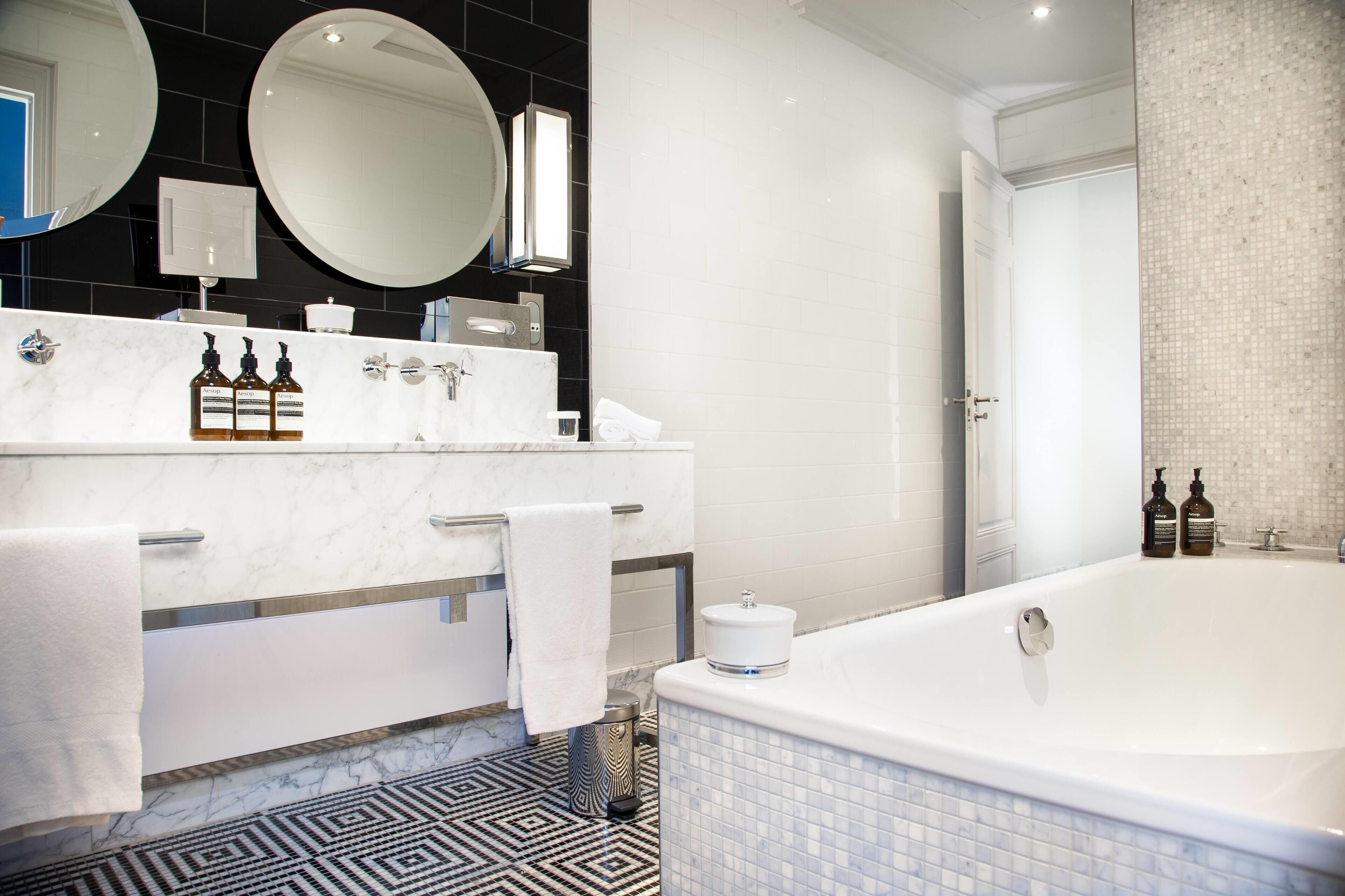 Un baño moderno con una bañera grande, un tocador de mármol, dos espejos y un suelo estampado.