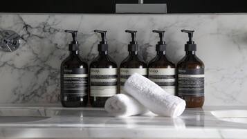 Um banheiro com bancada de mármore, cinco frascos de produtos de cuidados com a pele Aesop e uma toalha enrolada.