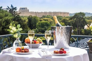 A table set with a bottle of champagne, glasses, fruit, and a vase of flowers, with a view of a historic building in the background.