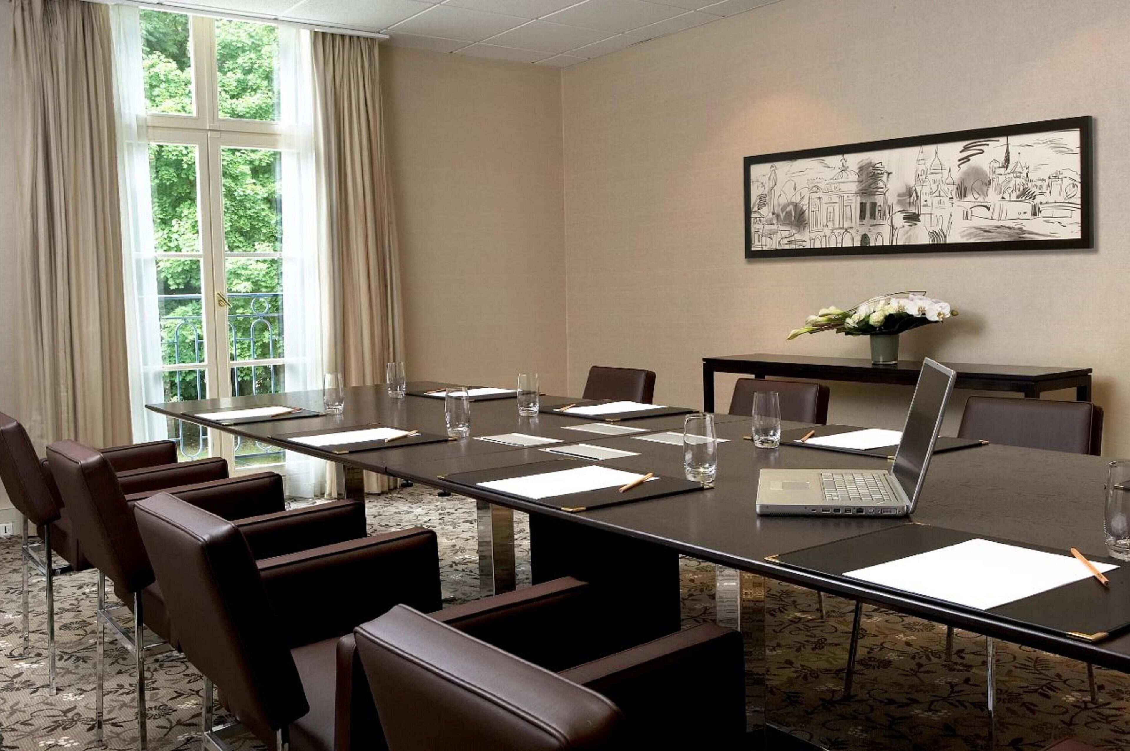 A conference room with a long table, chairs, a laptop, and a framed picture on the wall.