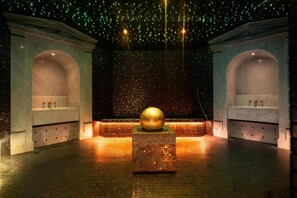 A spacious lobby with a central decorative gold sphere on a pedestal, flanked by two marble sinks with vases.